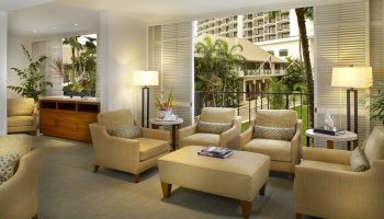 Halekulani Hotel living room. Gay-friendly hotel lounge area with armchairs, lamps, and a view of the tropical garden. Luxury travel in Honolulu.