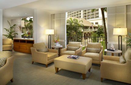 Halekulani Hotel living room. Gay-friendly hotel lounge area with armchairs, lamps, and a view of the tropical garden. Luxury travel in Honolulu.
