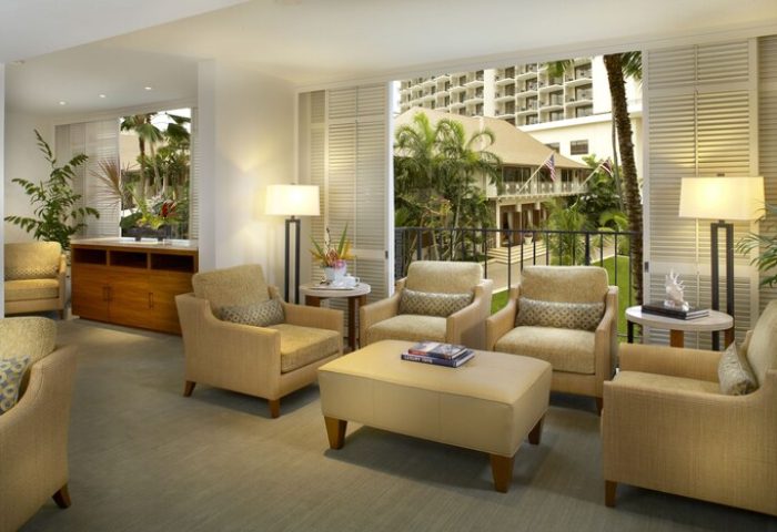 Halekulani Hotel living room. Gay-friendly hotel lounge area with armchairs, lamps, and a view of the tropical garden. Luxury travel in Honolulu.
