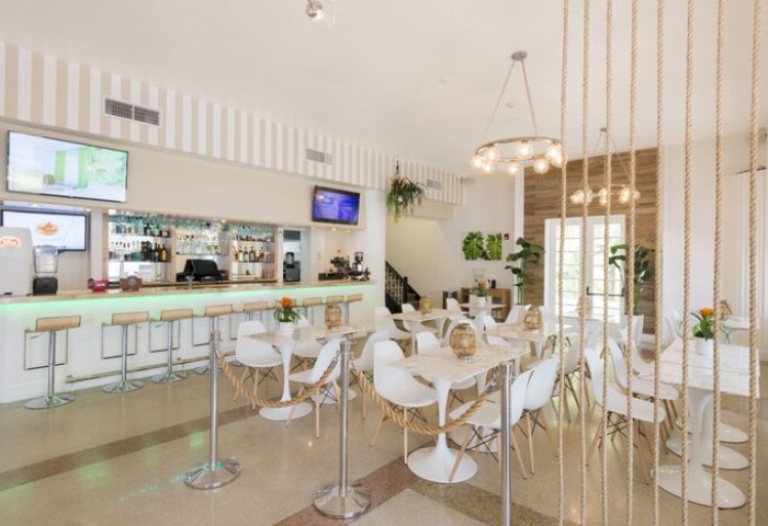 President Hotel's bar and dining area, a gay-friendly hotel. Modern decor with white tables, bar stools, and rope accents. TVs and a fully stocked bar.