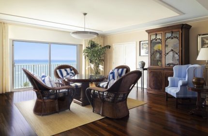 Kahala Hotel and Resort gay-friendly suite. Ocean view, wicker chairs, and blue accents create a luxurious, welcoming space for LGBTQ+ travelers.