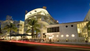 Strand Ocean Drive Suites, a gay-friendly hotel. Art Deco building at night with palm trees. Ideal for gay men's travel to Miami Beach.