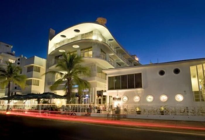 Strand Ocean Drive Suites, a gay-friendly hotel. Art Deco building at night with palm trees. Ideal for gay men's travel to Miami Beach.