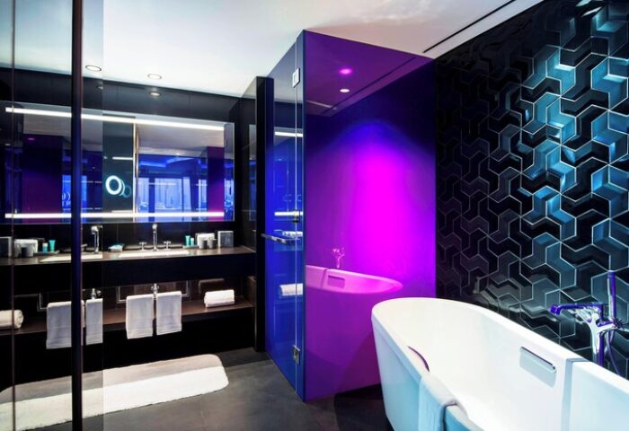 W Dubai - The Palm gay-friendly hotel bathroom. Modern design with a bathtub, vanity, and stylish blue and purple lighting.