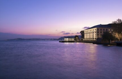 Shangri-La Bosphorus, Istanbul, a gay-friendly hotel, at dusk. The hotel's lights reflect on the Bosphorus strait. A luxurious gay travel destination.