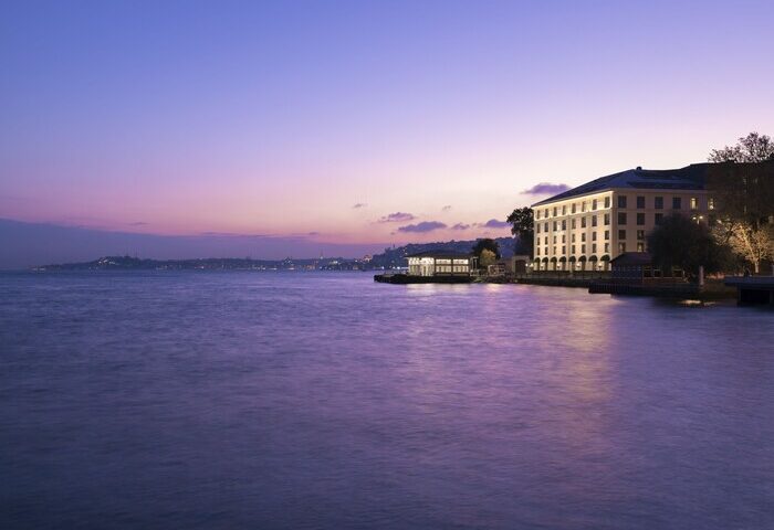 Shangri-La Bosphorus, Istanbul, a gay-friendly hotel, at dusk. The hotel's lights reflect on the Bosphorus strait. A luxurious gay travel destination.