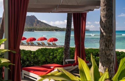 Sheraton Waikiki Beach Resort view of Diamond Head from a cabana. Red umbrellas and lounge chairs on the beach. Gay-friendly hotel.