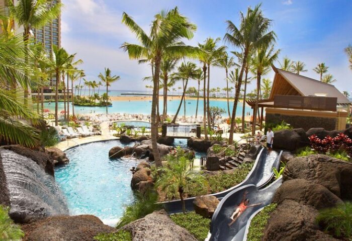 Hilton Hawaiian Village Waikiki Beach Resort pool and waterslide. Gay-friendly hotel with beach access, palm trees, and lagoon views.