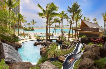 Hilton Hawaiian Village Waikiki Beach Resort pool and waterslide. Gay-friendly hotel with beach access, palm trees, and lagoon views.