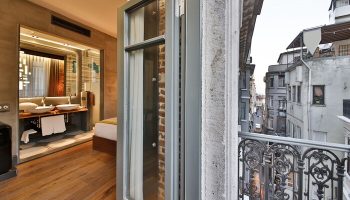 Hotel The Public, a special category gay-friendly hotel. Balcony view of city streets. Interior shows modern bathroom with double sinks and wood floors.