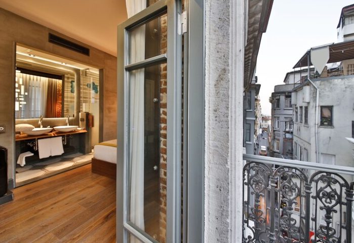 Hotel The Public, a special category gay-friendly hotel. Balcony view of city streets. Interior shows modern bathroom with double sinks and wood floors.