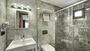 The Fox Hotel bathroom. Gay-friendly hotel features a modern shower, toilet, sink, and mirror. Marble walls add a touch of luxury.