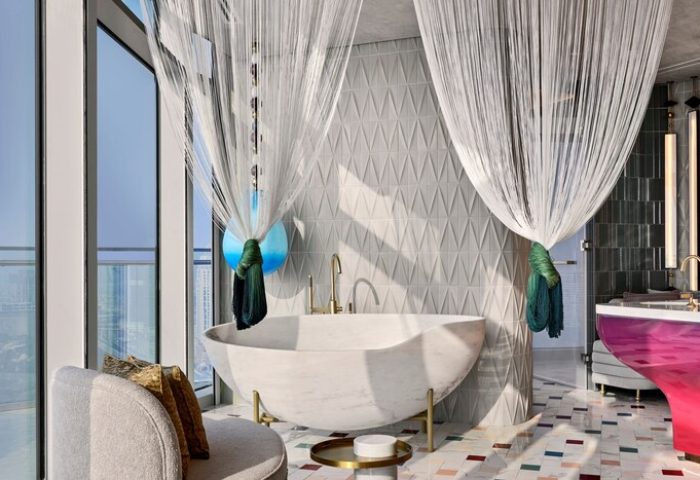 W Dubai - Mina Seyahi gay-friendly hotel bathroom. Modern design with a marble tub, sheer curtains, and colorful accents. Luxury gay travel.