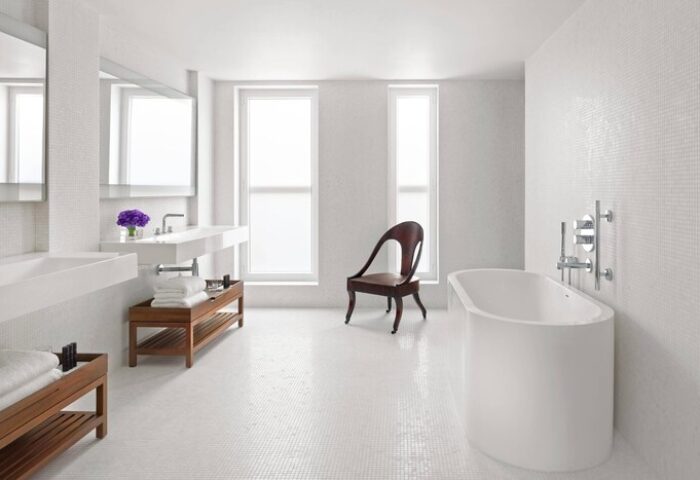 The London EDITION gay-friendly hotel bathroom. White tile, tub, dual sinks, wood chair, and natural light. A luxury travel experience.