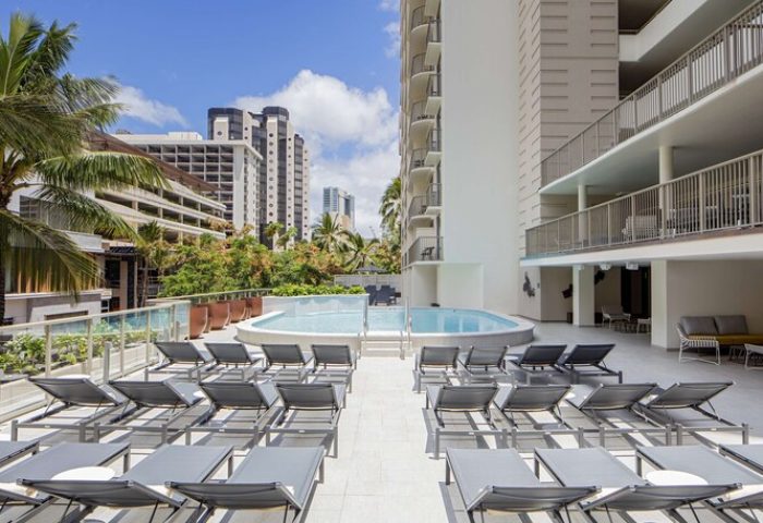 Hilton Garden Inn Waikiki Beach pool and lounge chairs. Gay-friendly hotel in Hawaii. Travel advice for gay men. Palm trees and city view.