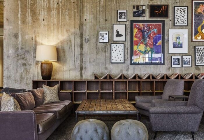 The Hoxton, Holborn hotel interior. Gay-friendly hotel lounge with concrete wall, art, sofa, chairs, and wooden table. Modern design.