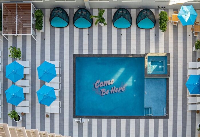 OHANA Waikiki East by OUTRIGGER pool aerial view. Gay-friendly hotel with blue umbrellas, lounge chairs, and Came Be Here pool art.