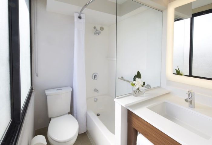Holiday Inn Express Waikiki gay-friendly hotel bathroom. Features a toilet, bathtub with shower, sink, and illuminated mirror.