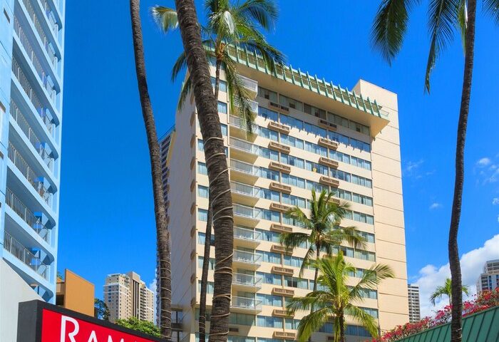 Ramada Plaza by Wyndham Waikiki, a gay-friendly hotel. Exterior view with palm trees and blue sky. Ideal for gay travel in Waikiki, Hawaii.