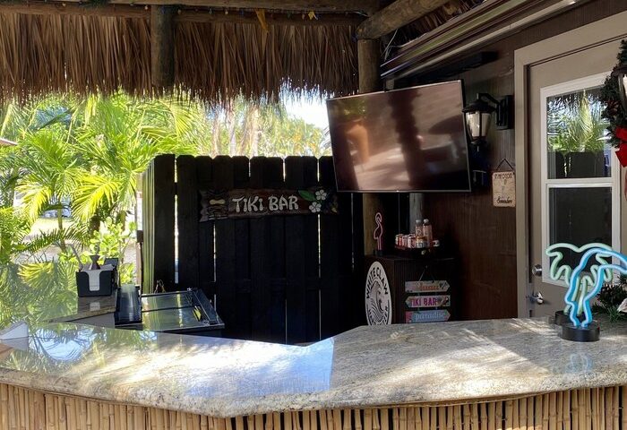 Tiki bar at a gay-friendly resort. Thatched roof, bamboo bar with stools, TV, and neon palm tree. A relaxing spot for gay men's travel.