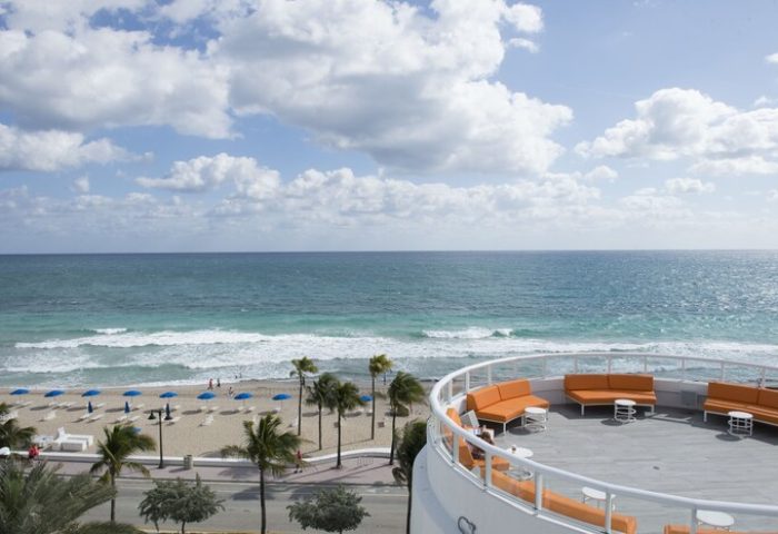 Hilton Fort Lauderdale Beach Resort view. Gay-friendly hotel's rooftop lounge overlooking the beach and ocean. Palm trees and blue umbrellas.