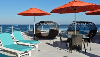 Gay-friendly hotel rooftop with ocean view. Lounge chairs, orange umbrellas, and stylish seating areas offer relaxation. A perfect gay travel getaway.