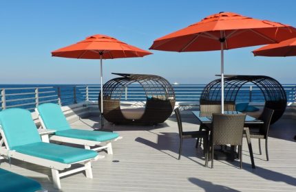 Gay-friendly hotel rooftop with ocean view. Lounge chairs, orange umbrellas, and stylish seating areas offer relaxation. A perfect gay travel getaway.