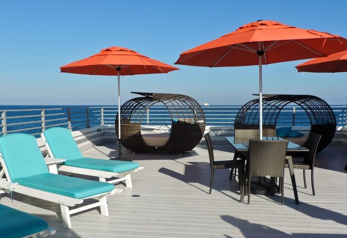 Gay-friendly hotel rooftop with ocean view. Lounge chairs, orange umbrellas, and stylish seating areas offer relaxation. A perfect gay travel getaway.
