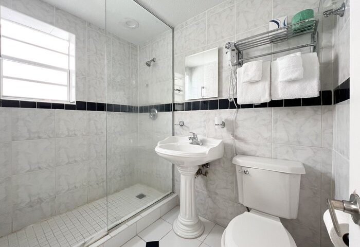 La Casa Hotel gay-friendly bathroom with shower, sink, and toilet. White tile and black accents. Ideal for gay men travel.