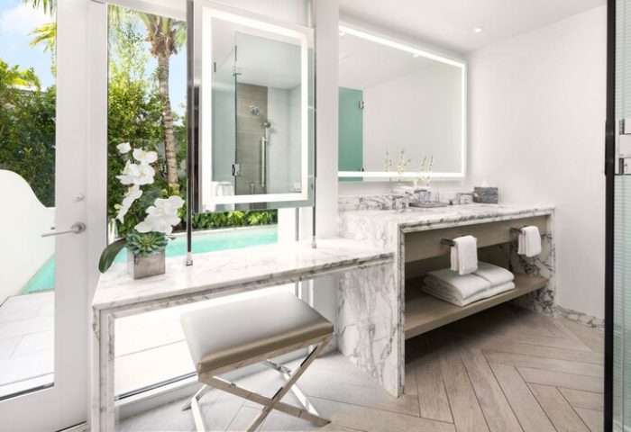H2O Suites adults only gay-friendly hotel bathroom. Marble vanity, illuminated mirror, stool, and view of the pool. Upscale gay travel.