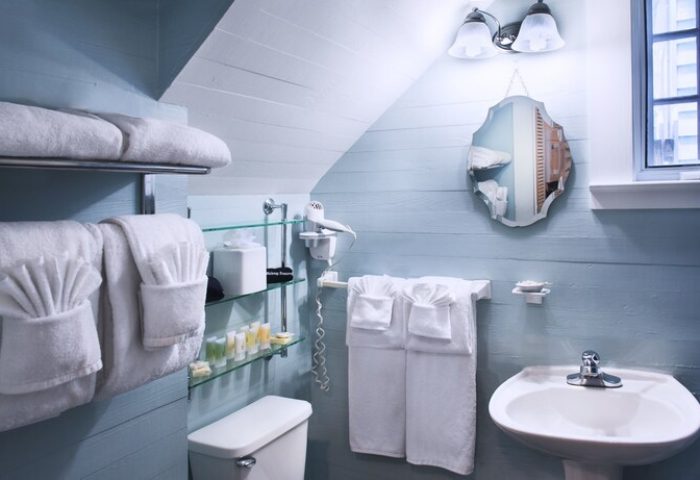 Island City House gay-friendly hotel bathroom. Light blue walls, white towels, sink, toilet, mirror, and toiletries on glass shelves.