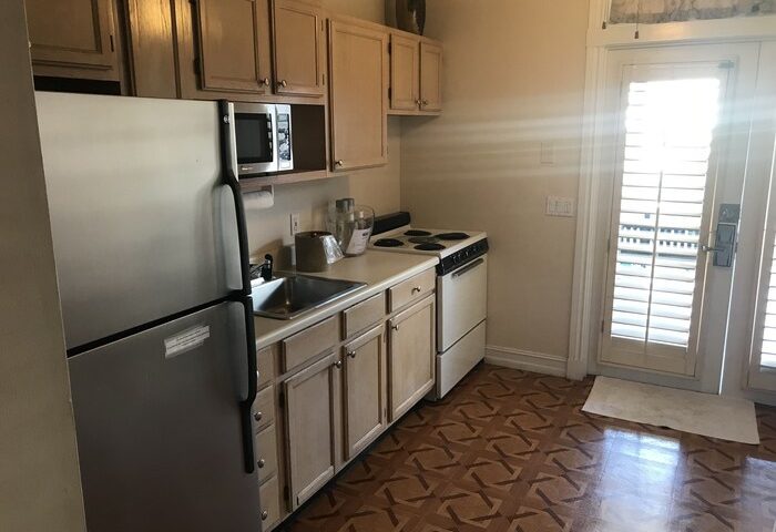 Kitchen in New Orleans house at a gay-friendly hotel. Stainless steel fridge, oven, and microwave. Cabinets, sink, and patterned floor.