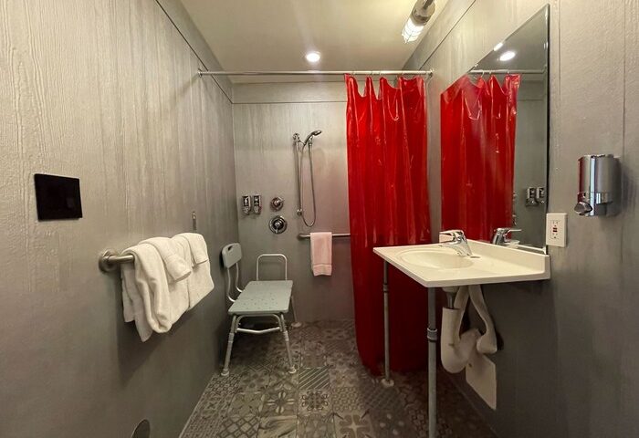 Hotel Gaythering gay-friendly hotel bathroom with red shower curtain, sink, and accessible shower seat. All adults welcome.