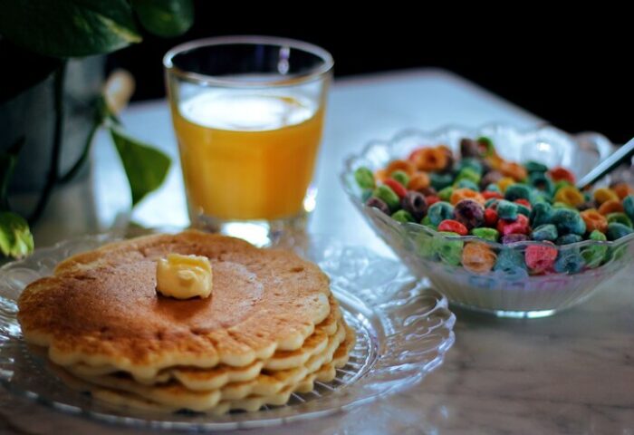 Breakfast at gay-friendly hotel: Stack of pancakes with butter, orange juice, and a bowl of colorful cereal. Delicious morning meal.