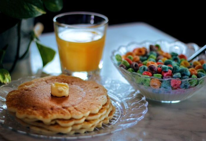 Breakfast at gay-friendly hotel: Stack of pancakes with butter, orange juice, and a bowl of colorful cereal. Delicious morning meal.