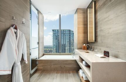 EAST Miami gay-friendly hotel bathroom. Bathtub by a large window with city view. Robe, sink, and toiletries. Modern design.