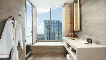 EAST Miami gay-friendly hotel bathroom. Bathtub by a large window with city view. Robe, sink, and toiletries. Modern design.