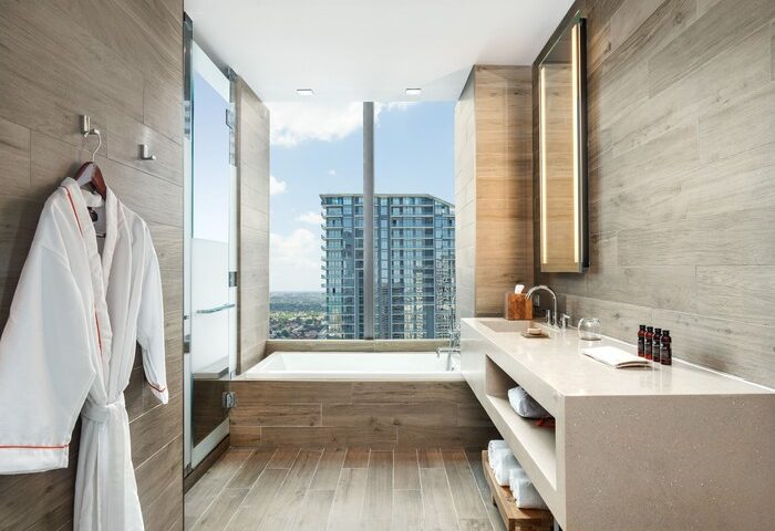 EAST Miami gay-friendly hotel bathroom. Bathtub by a large window with city view. Robe, sink, and toiletries. Modern design.