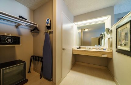 Hyatt Regency Miami gay-friendly hotel room detail. Closet with safe, iron, ironing board, and fridge. Bathroom area with large mirror and counter.