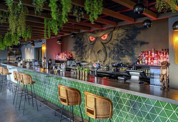 25hours Hotel One Central bar area. Green tiled bar front, monkey mural, hanging plants. Gay-friendly hotel, travel advice for gay men.