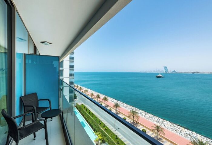 Aloft Palm Jumeirah gay-friendly hotel balcony view. Ocean, Dubai skyline, and chairs. Perfect for gay travel and relaxation.