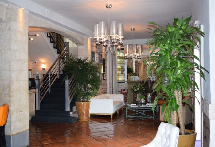 Hotel Shelley's interior: Gay-friendly hotel lobby with plants, chandeliers, and seating. A staircase is visible. Welcoming space for gay travelers.