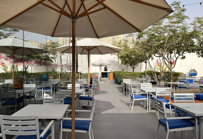 Outdoor dining area at Aloft Me'aisam, Dubai. Tables with blue chairs under umbrellas. Gay-friendly hotel for gay men travel advice.