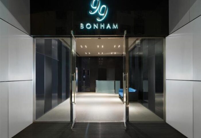 Entrance to 99 Bonham, a gay-friendly hotel. Modern design with glass doors and a neon sign. A welcoming space for gay travelers.