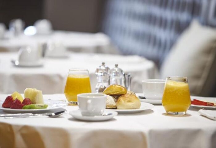 Breakfast at 9HOTEL MERCY, a gay-friendly hotel. Table setting with juice, coffee, fruit, and rolls. Ideal for gay men's travel.
