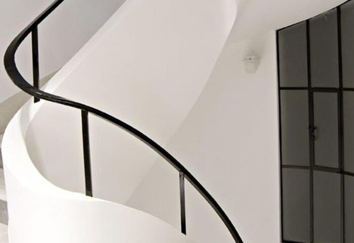 Interior of A For Athens Hotel, a gay-friendly hotel. White spiral staircase with black metal railing and a window with black frame.