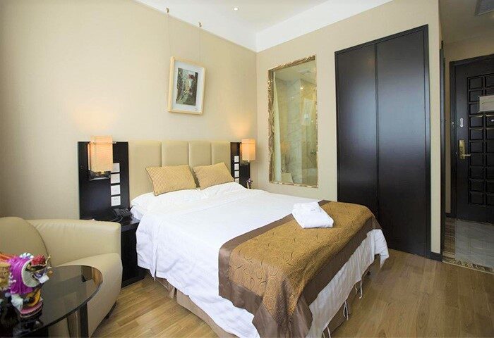 AC Embassy Hotel gay-friendly room. Queen bed with beige headboard, sofa, and closet. Modern design, comfortable stay. Gay travel.