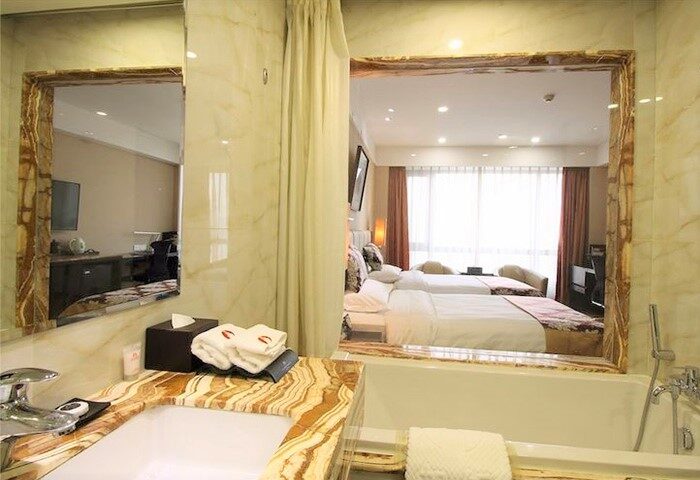 AC Embassy Hotel's bathroom with marble accents, sink, and bathtub. Reflected in the mirror is a view of the gay-friendly hotel room with two beds.