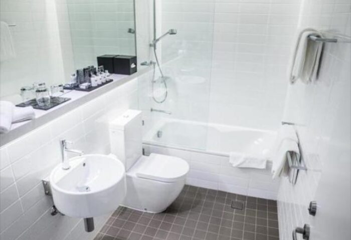 ADGE Apartments gay-friendly hotel bathroom. Features a white sink, toilet, bathtub, shower, and gray tiled floor. Modern design.