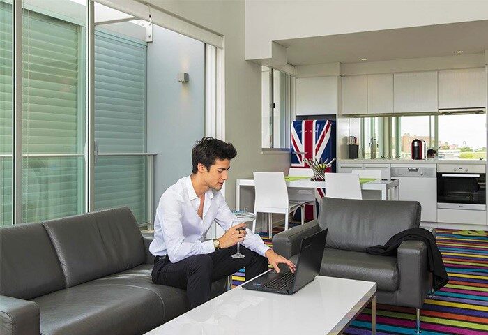 ADGE Apartments gay-friendly hotel: Man on laptop with wine in modern apartment. Kitchen with Union Jack fridge in background.